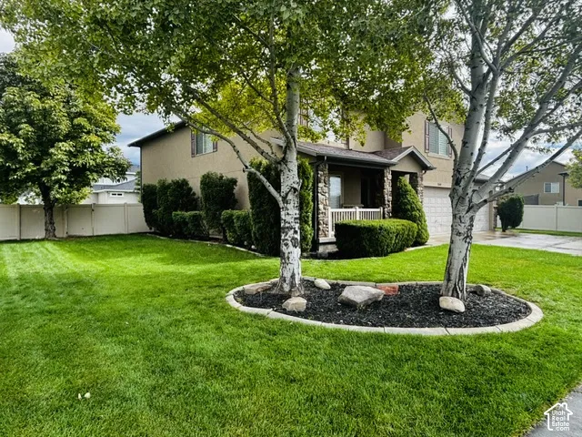 Two-story residence with a covered porch, stone accents, and a front yard with mature trees