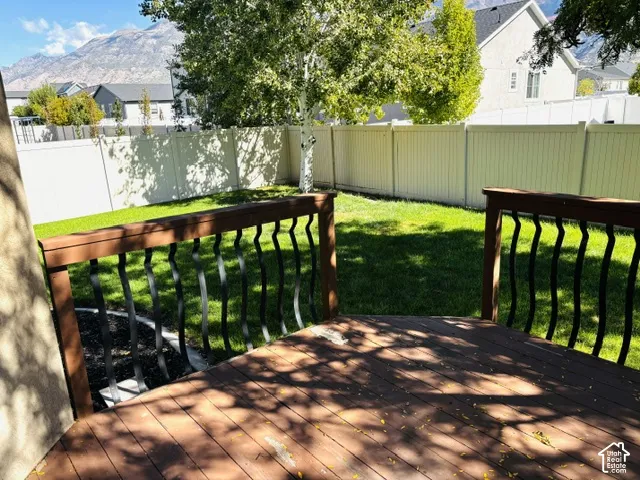 Wood-finish deck with wrought iron balusters overlooking a fenced backyard with a lawn and mature trees
