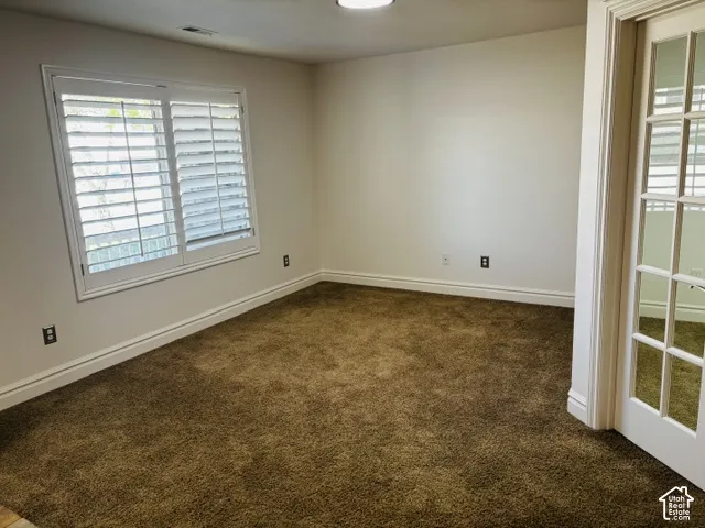 Plantation shutters on a large window, brown carpeting, white baseboards, and a white French door with glass panels
