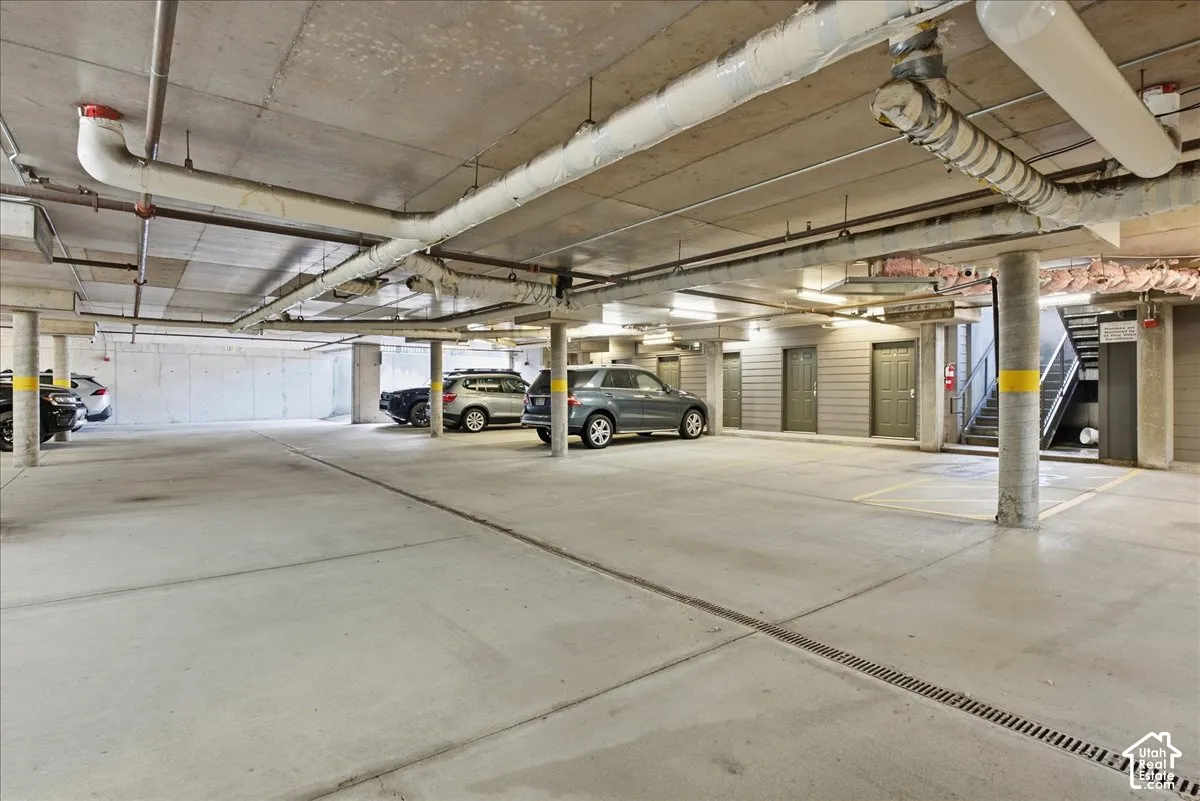 Concrete underground parking garage with exposed piping, structural columns, and multiple access doors
