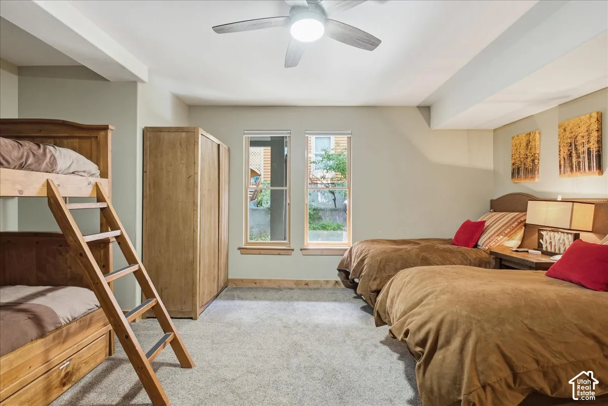 Carpeted flooring, two windows with wood trim, ceiling fan, and built-in wood bunk beds with ladder