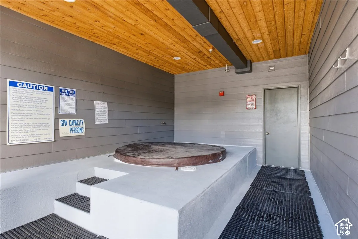 Built-in spa with integrated steps, overhead wood-finish ceiling, grey wall siding, recessed lighting, and a solid door