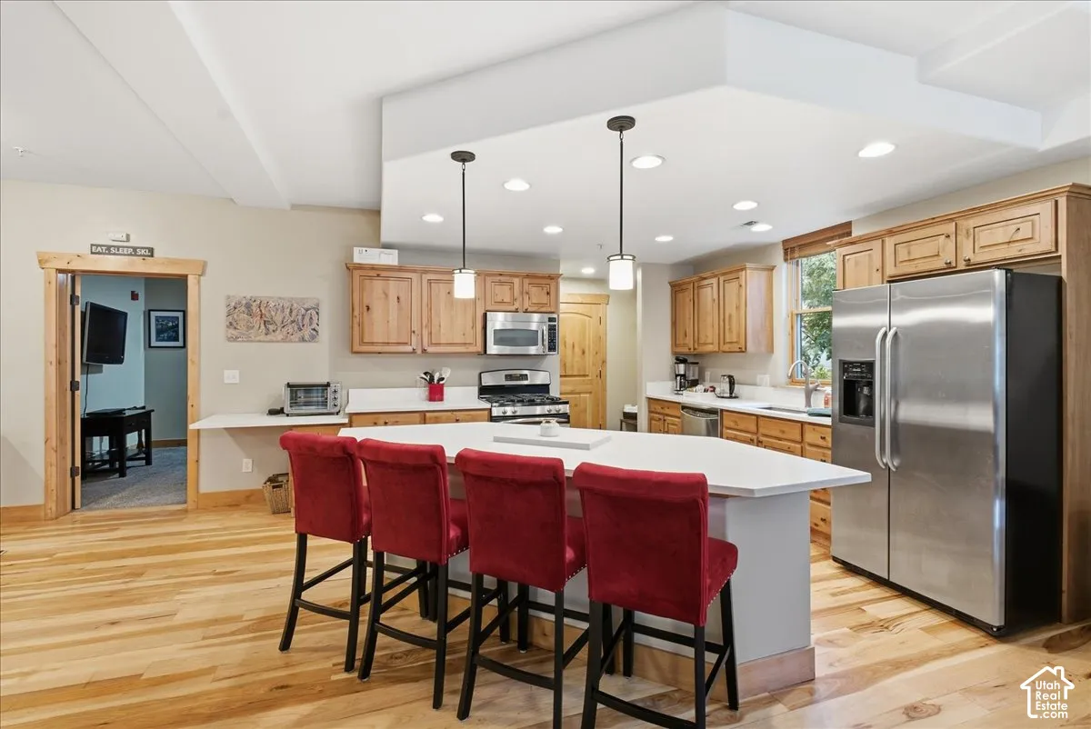 Kitchen featuring wood-finish flooring, light wood cabinetry, stainless steel appliances, and a central island with a solid surface countertop