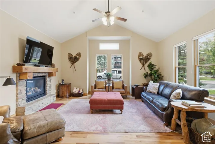 Vaulted ceilings, a stone-clad fireplace with a wood mantel, wood-finish flooring, and multiple windows