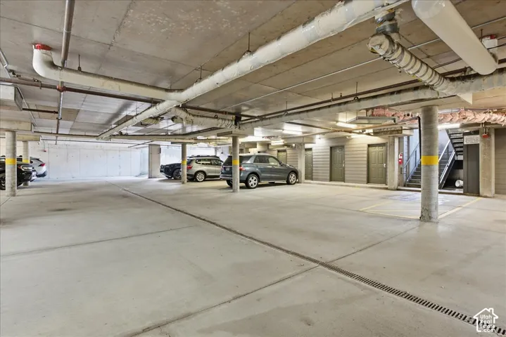 Concrete underground parking garage with exposed piping, structural columns, and multiple access doors