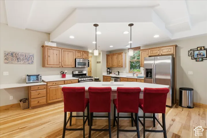 Kitchen featuring wood-finish cabinetry, stainless steel appliances, a center island with seating, recessed lighting, and wood-finish flooring