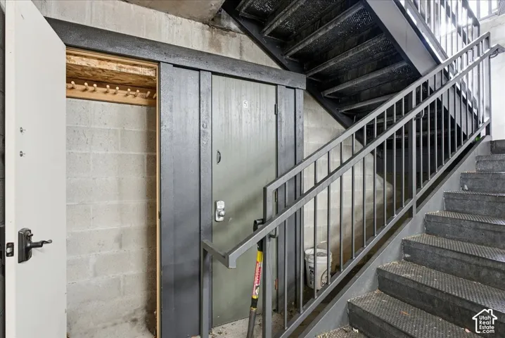 Concrete block walls with a wooden coat rack, a dark wood-finish sliding door, and a metal staircase featuring a gray handrail