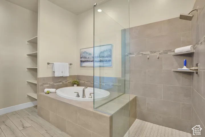 Freestanding soaking tub with tiled surround, walk-in shower with glass enclosure, built-in shower shelving, rainfall shower head, and wood-finish flooring