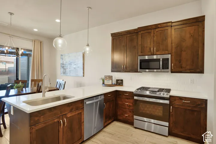 Kitchen featuring wood-finish cabinetry, stainless steel appliances, white subway tile backsplash, light-toned countertops, and wood-finish flooring