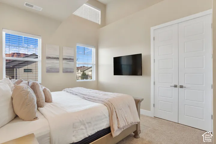 Vaulted ceilings with an upper transom window, two windows with blinds, light-toned carpeting, and double panel doors