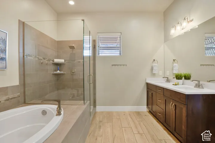 Tiled walk-in shower with a rain shower head, separate soaking tub, wood-finish flooring, dual vanity with undermount sinks, and a large mirror