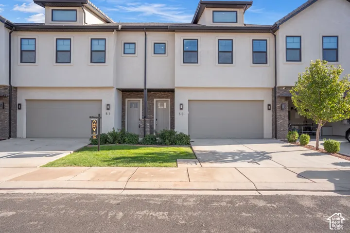 Stucco exterior with stone accents, integrated garage, and a dormer window feature