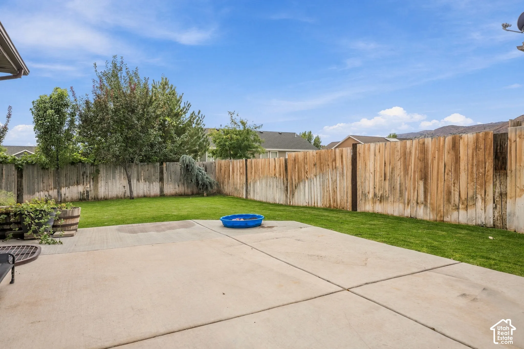 Expansive concrete patio with a manicured lawn and mature trees, enclosed by a wooden privacy fence