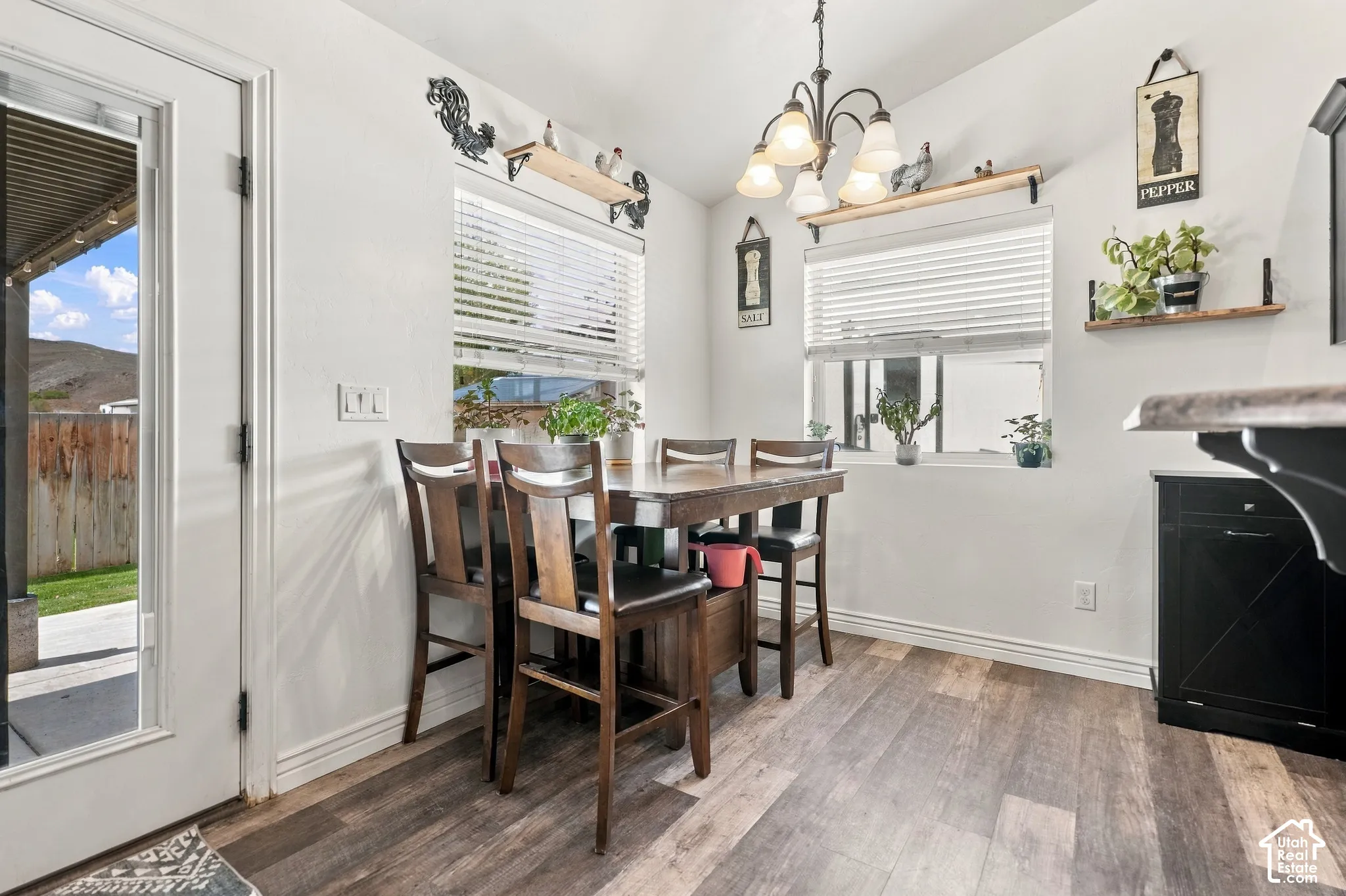 Bright dining area featuring a wood-finish table with upholstered chairs, pendant lighting fixture, and abundant natural light from dual windows with plantation shutters