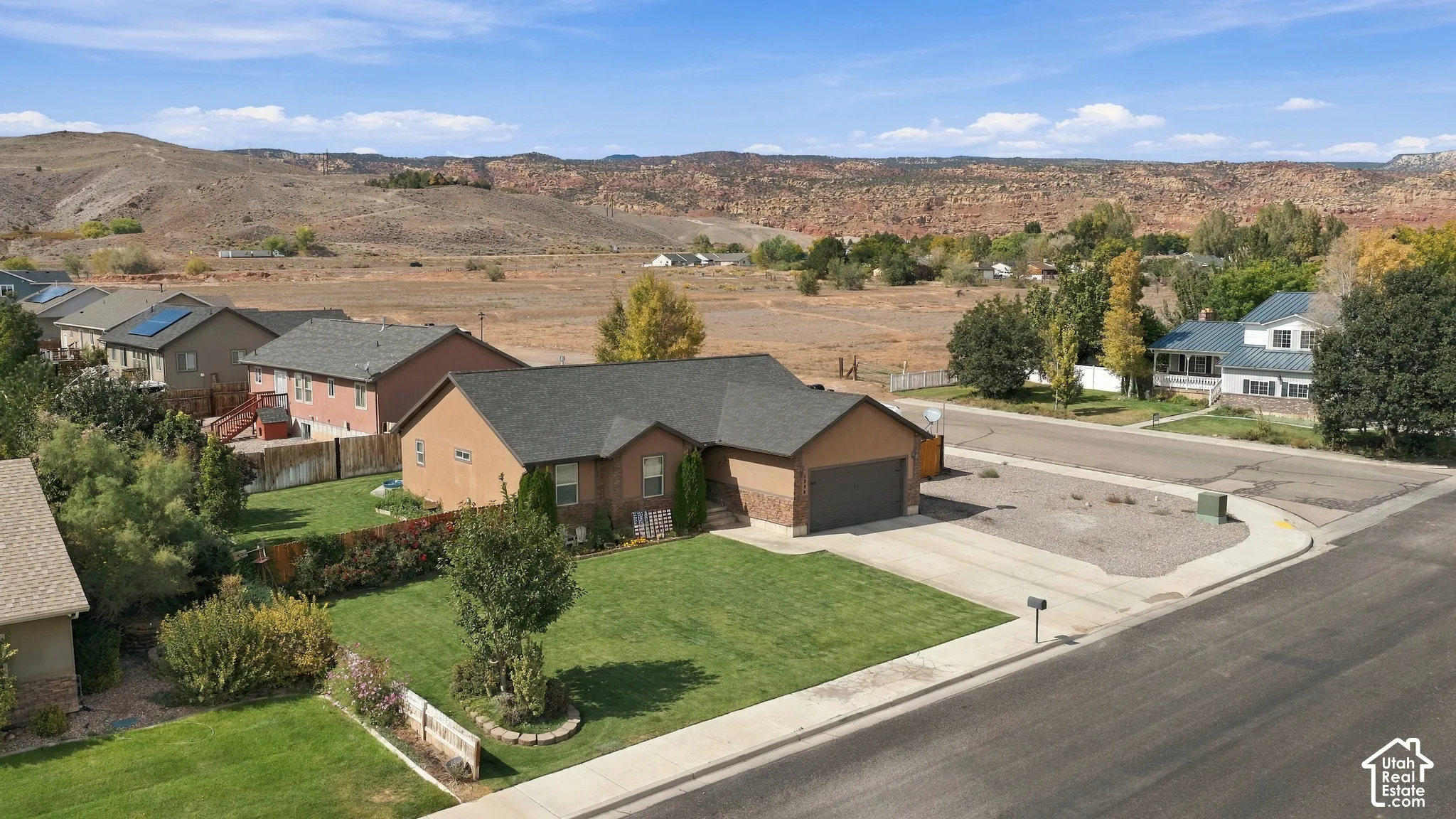 Single-story stucco exterior with an attached garage, featuring a front lawn and a visible backdrop of natural terrain