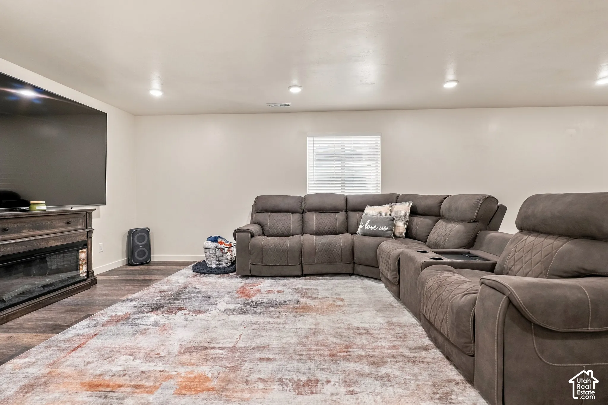 Wood-finish flooring with recessed lighting, a window featuring horizontal blinds, and a built-in media console with an electric fireplace