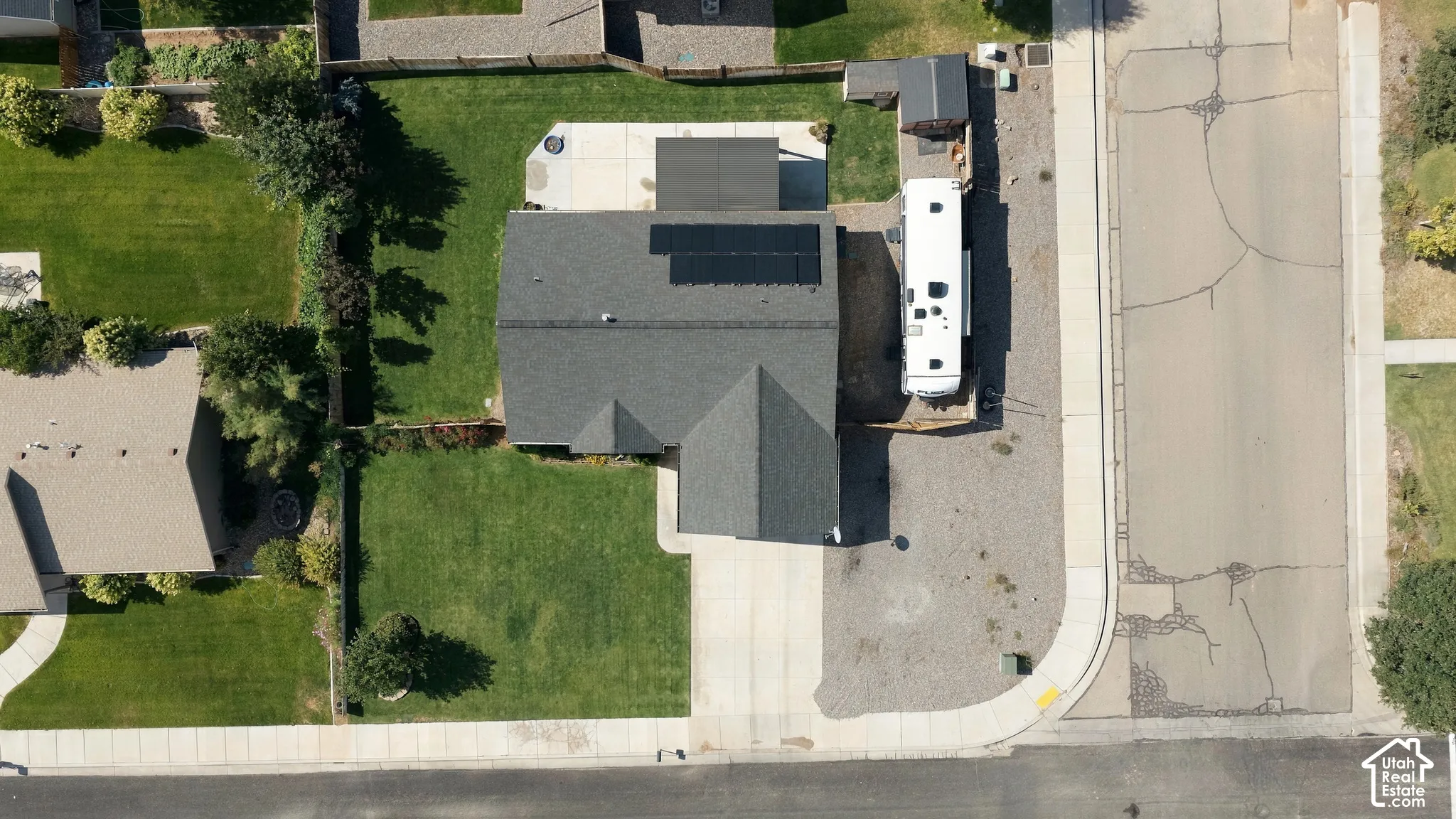 Modern home featuring a professionally installed solar panel array on the roof, expansive manicured lawn with mature landscaping, generous driveway with concrete paving, and clean architectural lines with mixed exterior finishes including dark asphalt shi