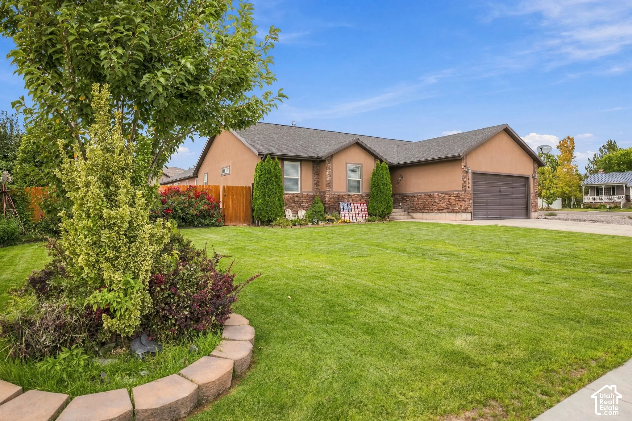 Stucco and stone exterior, attached garage, manicured lawn, paved driveway, mature landscaping