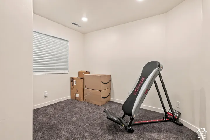 Recessed lighting illuminates the room, featuring a window with white blinds and dark gray carpeting