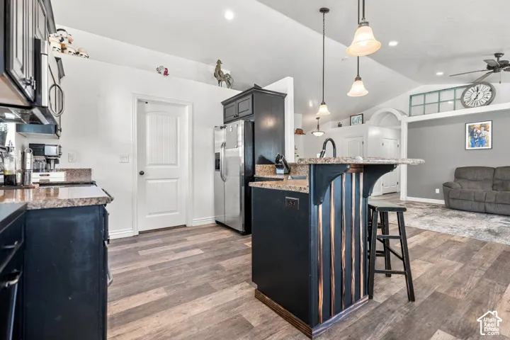 Kitchen featuring wood-finish flooring, dark cabinetry, light-toned countertops, and a central island with pendant lighting