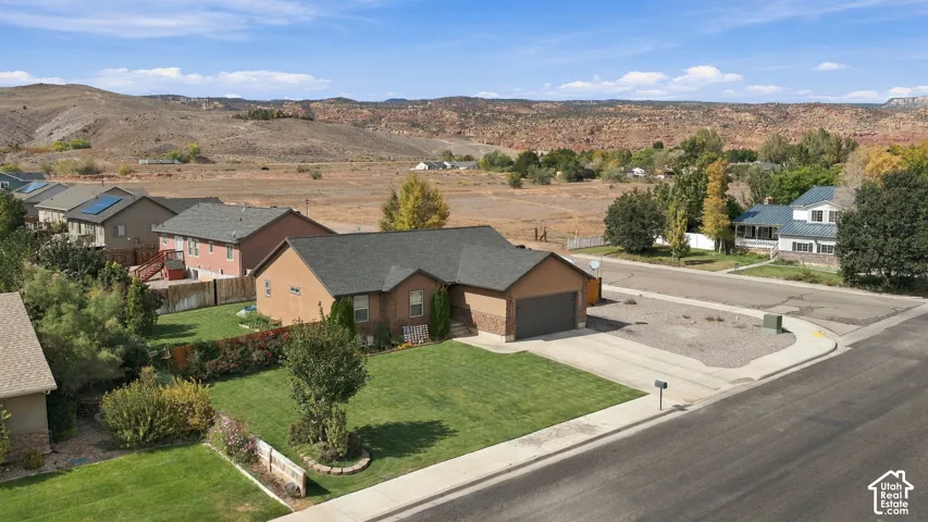Single-story stucco exterior with an attached garage, featuring a front lawn and a visible backdrop of natural terrain