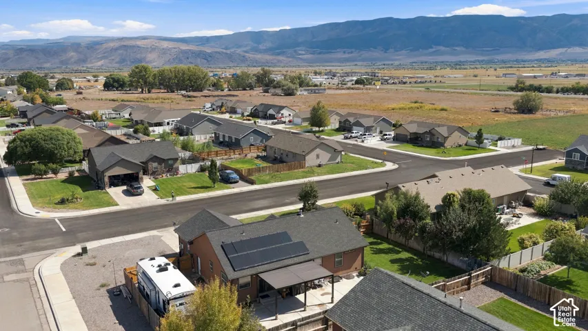 Aerial view showcasing this residential property situated on a generous lot with mature landscaping, paved driveway, and modern roofing