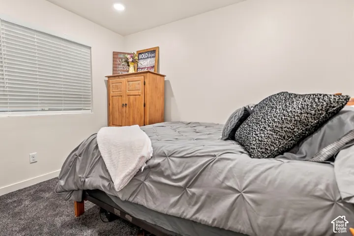 Recessed ceiling lighting illuminates the space, featuring white walls, a single window with blinds, and dark gray carpeting