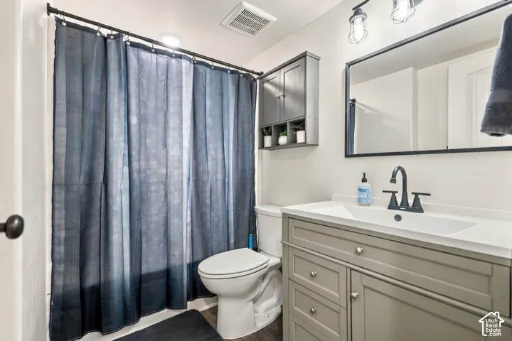 Bathroom featuring a single-sink vanity with light gray cabinetry, a rectangular mirror with a black frame, black-finished hardware, a wall-mounted storage cabinet, and wood-finish flooring