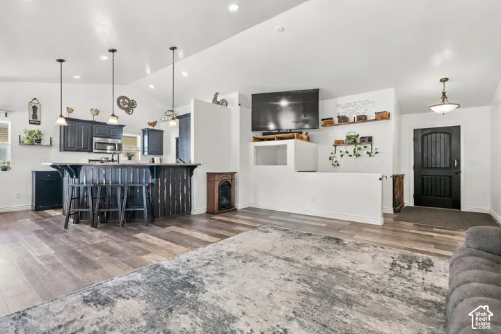 Vaulted ceiling, wood-finish flooring, kitchen island with seating, stainless steel appliances, and a dark wood front door