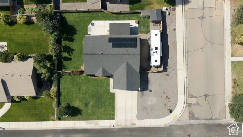 Modern home featuring a professionally installed solar panel array on the roof, expansive manicured lawn with mature landscaping, generous driveway with concrete paving, and clean architectural lines with mixed exterior finishes including dark asphalt shi