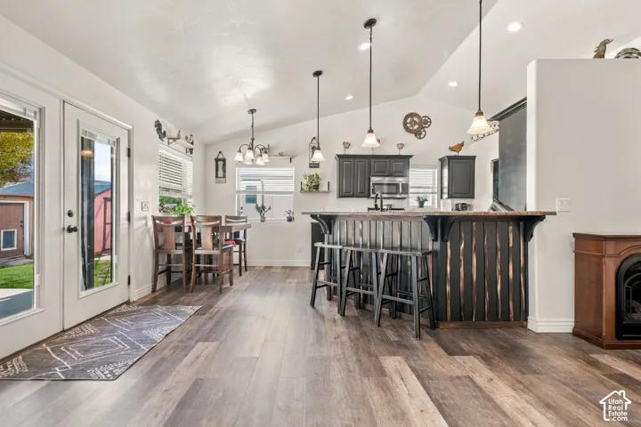 Vaulted ceilings, wood-finish flooring, dark wood-finish cabinetry, built-in breakfast bar, and multiple pendant light fixtures