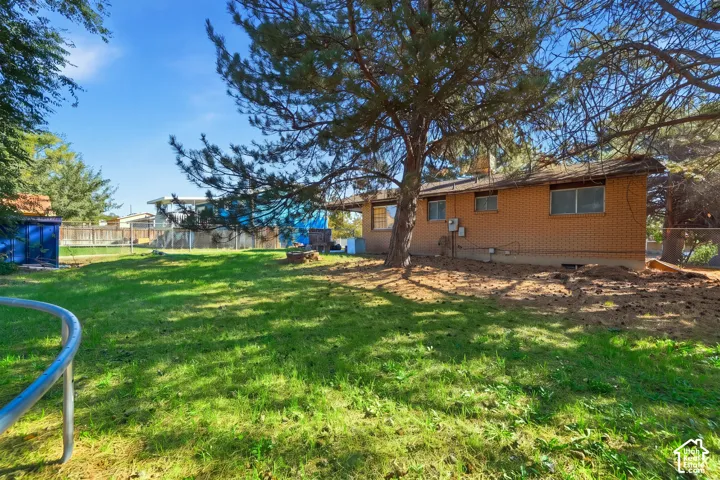 Expansive rear yard featuring green grass, mature trees, and a brick exterior with multiple windows