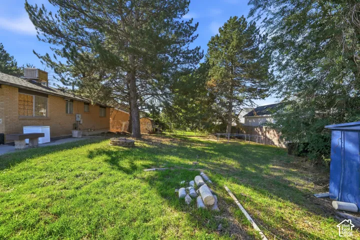 Expansive grassy yard featuring mature trees, a small shed, and a stone-lined fire pit