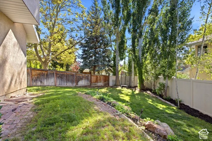 Expansive backyard featuring a manicured lawn, established perimeter trees, wood privacy fencing, a brick pathway, and a trellis