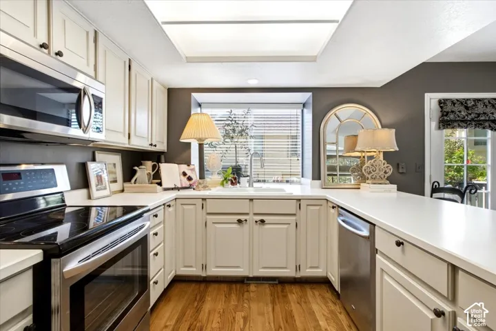 U-shaped kitchen featuring wood-finish flooring, white cabinetry with dark hardware, stainless steel appliances, white countertops, and a window above the sink