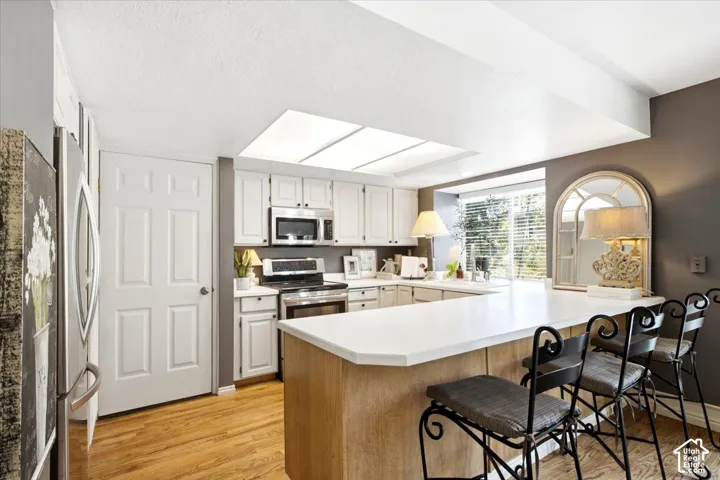 Kitchen featuring white cabinetry, stainless steel appliances, a breakfast bar, and wood-finish flooring