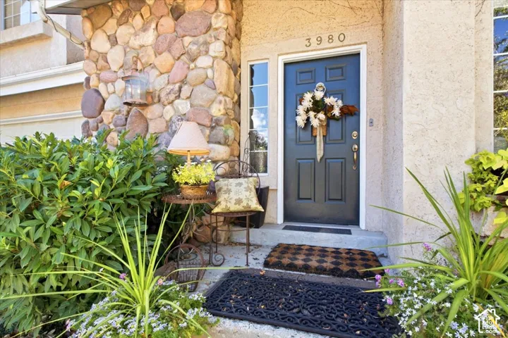 Stone column detailing, stucco exterior, paneled front door, sidelight window, and integrated landscaping