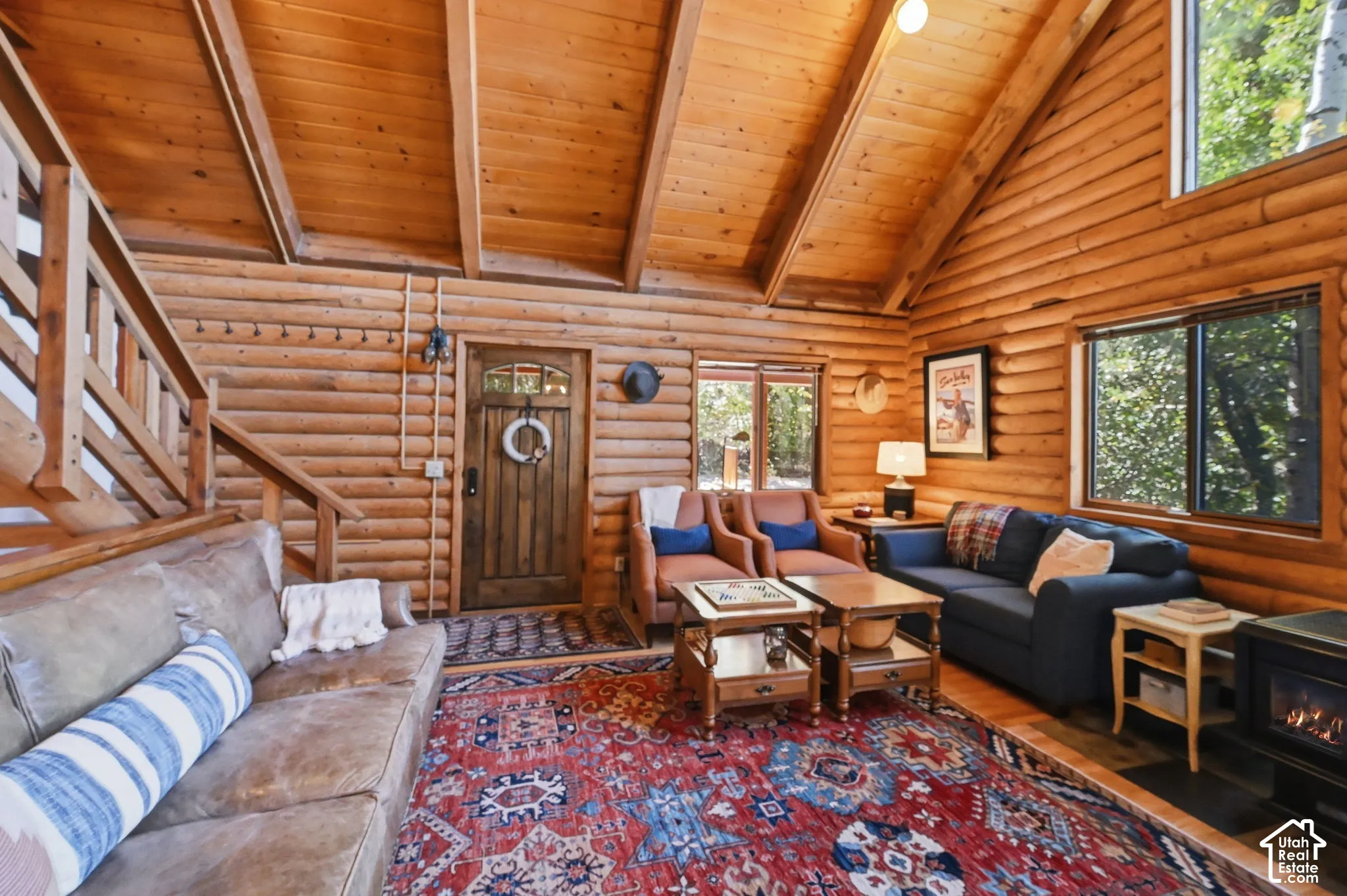 Vaulted wood-paneled ceiling, wood log walls, built-in staircase with wood railing, gas fireplace, and multiple windows