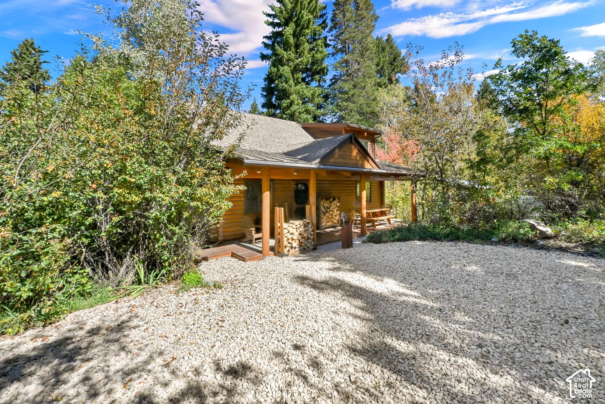 Wood-sided cabin exterior with a covered porch, gravel driveway, and surrounding natural foliage