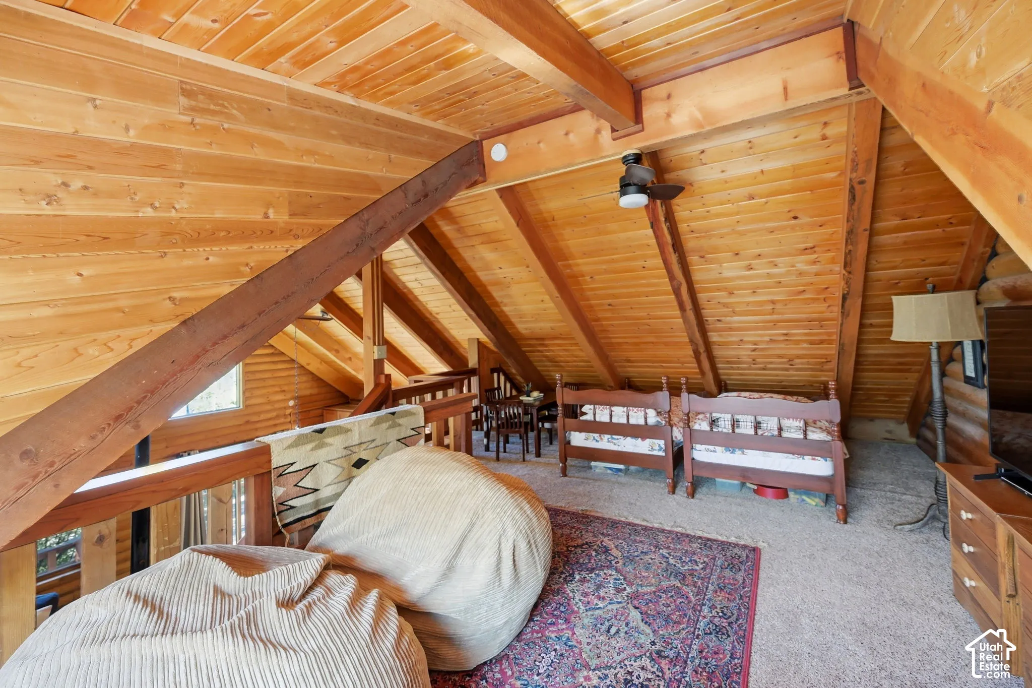 Vaulted wood-paneled ceiling with exposed beams, wood-finish railing, ceiling fan, and carpeted flooring