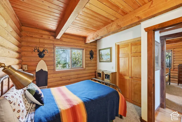 Log-style wall construction, wood-finish ceiling, exposed wood beams, wood-trimmed window, and wood-panel bifold closet doors