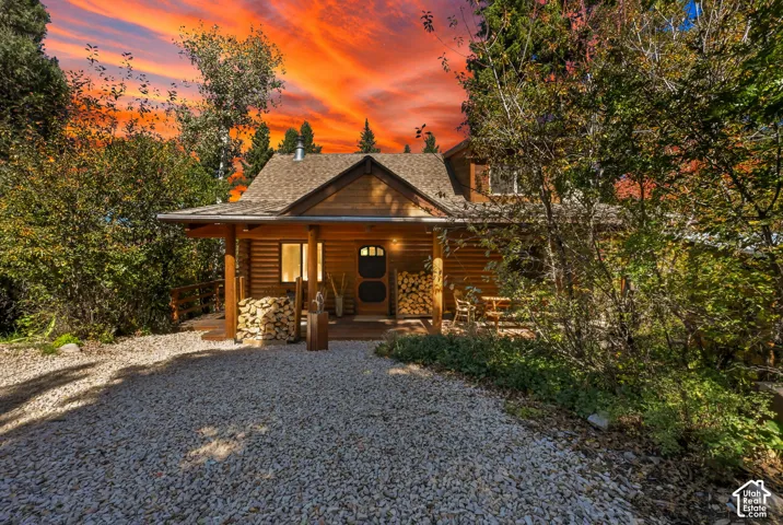 Gravel driveway leading to a log cabin exterior with a covered porch and wood siding