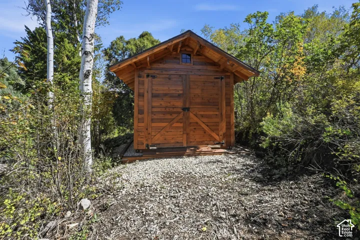 Wood-sided outbuilding featuring a gabled roof, a transom window, and a gravel-covered base