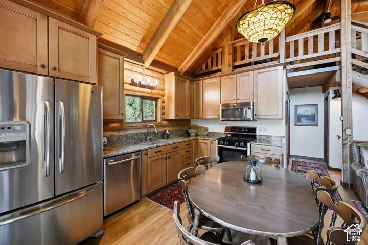 Kitchen featuring stainless steel appliances, wood-finish cabinetry, granite-finish countertops, wood-finish flooring, and a vaulted wood-beam ceiling