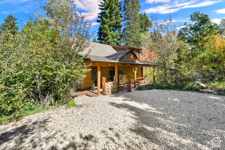Wood-sided cabin exterior with a covered porch, gravel driveway, and surrounding natural foliage