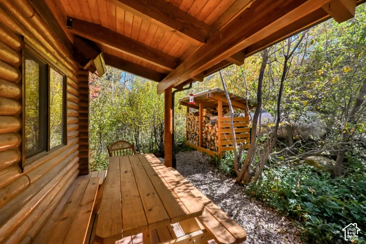 Log cabin exterior featuring a covered porch with exposed wood beams, a wood-sided wall, a window, and a gravel-covered area with a wood storage shed