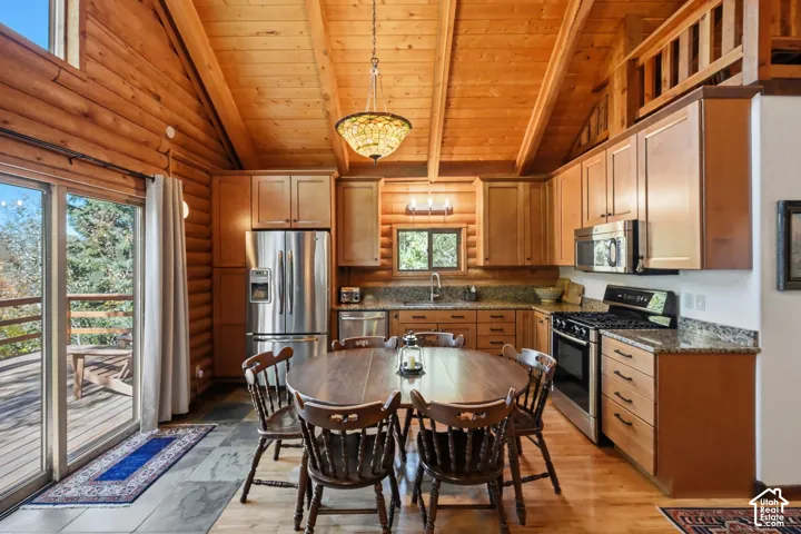 Kitchen featuring wood-finish cabinetry, stainless steel appliances, granite countertops, and a wood-beamed vaulted ceiling