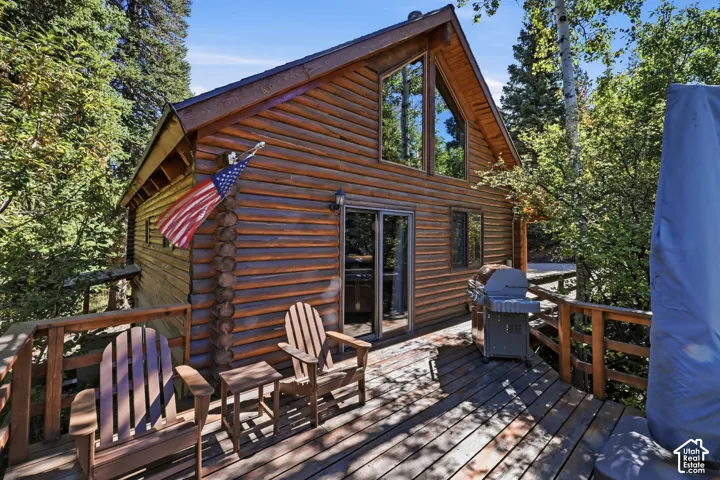 Expansive wood deck with a timber railing, featuring direct access to the interior through glass sliding doors, and a natural wood-sided exterior with large upper-story windows