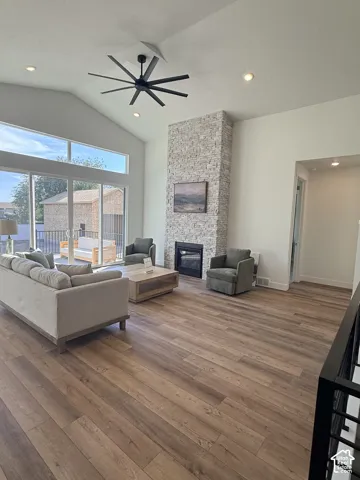 Vaulted ceiling with a contemporary ceiling fan, stone-clad fireplace with a built-in firebox, wood-finish flooring, recessed lighting, and large sliding glass doors