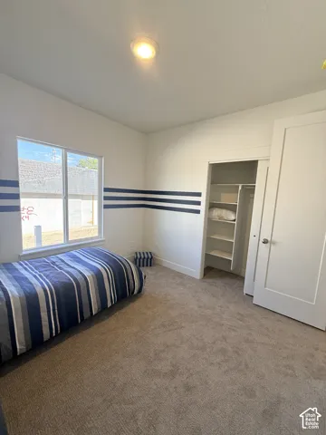 Recessed ceiling lighting, carpeted flooring, and a window with natural light complement the built-in closet with shelving and white paneled doors